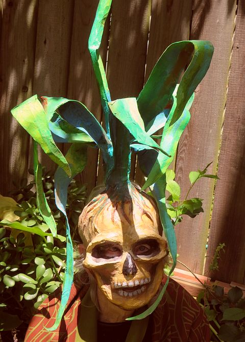 Jenny Badger Sultan in a skull mask from which corn stalks grow. Click to enlarge